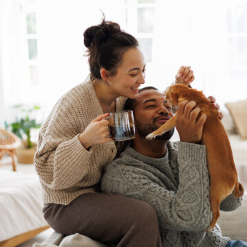Cheerful young interracial couple with coffee playing with chihuahua dog at home