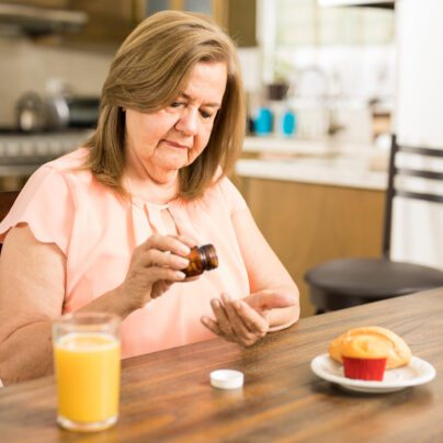 older woman taking medication with juice