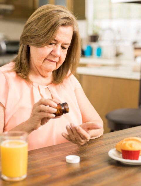 older woman taking medication with juice