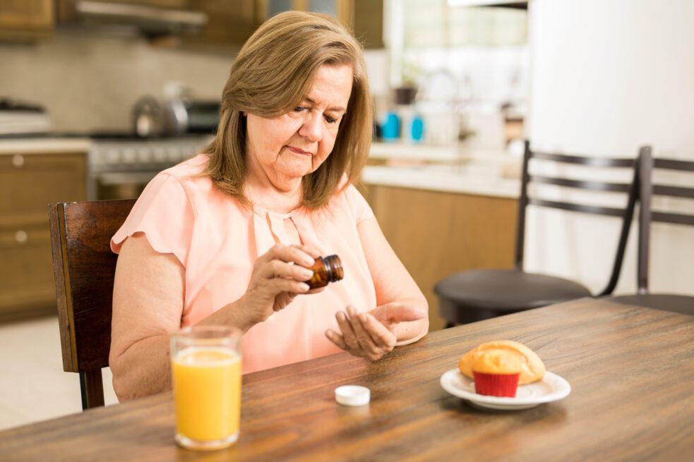 older woman taking medication with juice