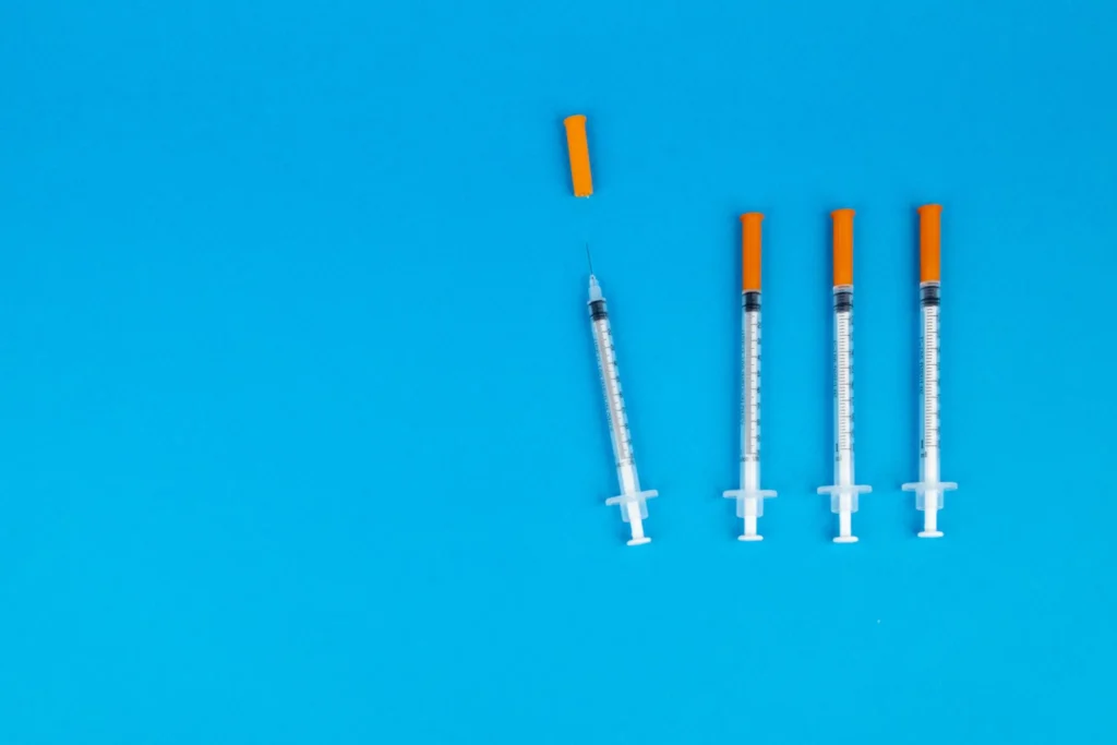 Four syringes with orange caps on a blue background
