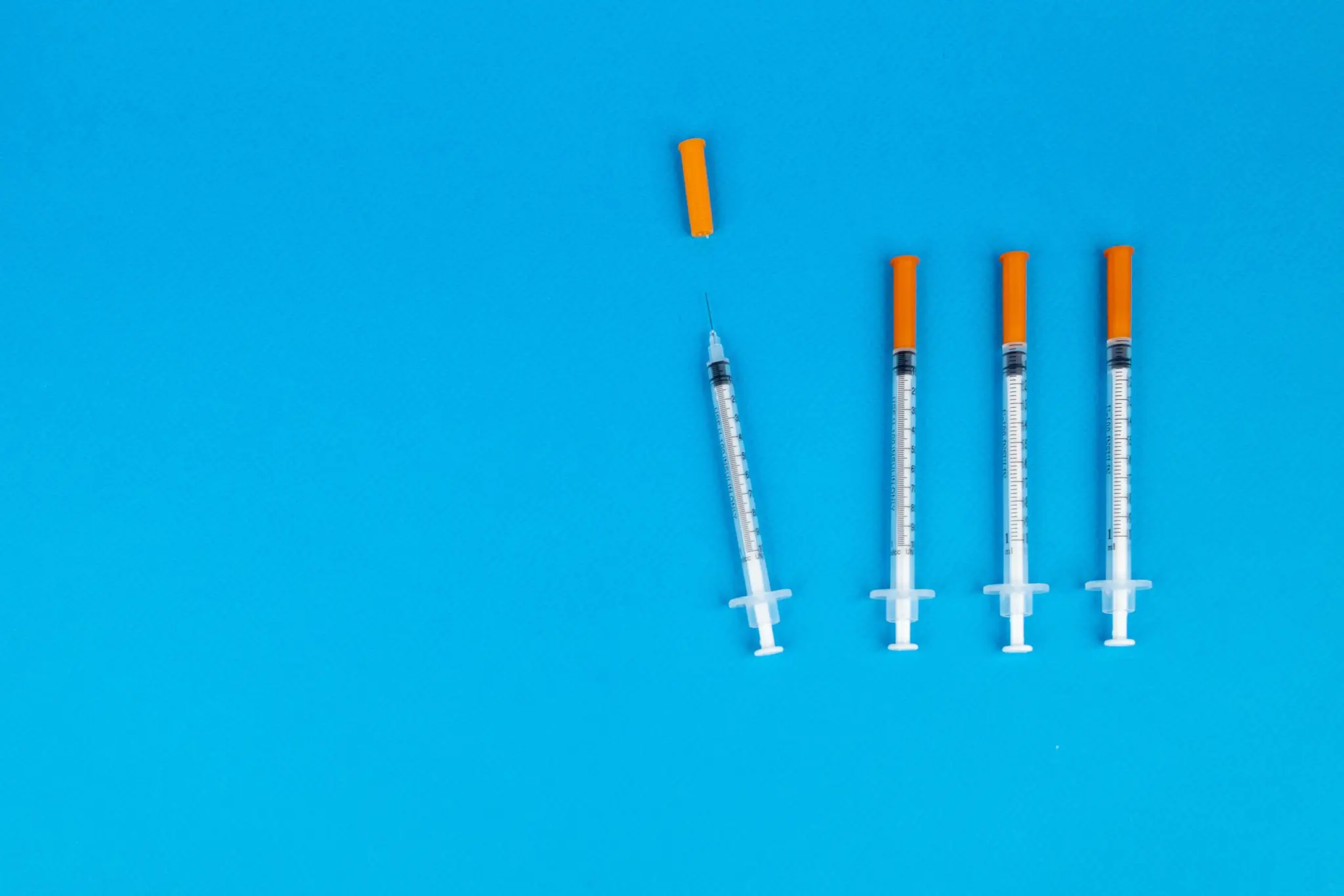 Four syringes with orange caps on a blue background